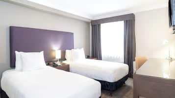 A hotel room with two beds, a desk, and a large window with curtains.