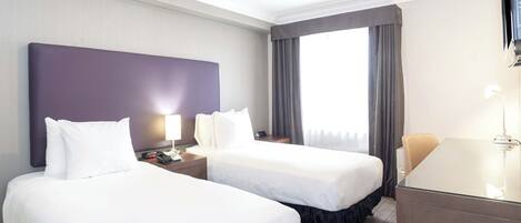 A hotel room with two beds, a desk, and a large window with curtains.