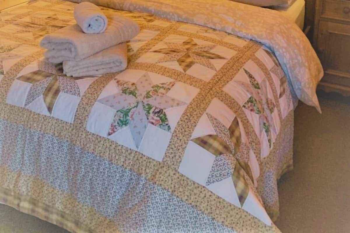 A wooden-paneled bedroom with a bed, two nightstands, a mirror, and a quilted bedspread.
