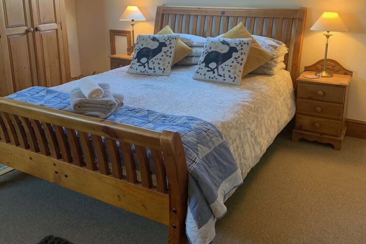 A bedroom with a sloped ceiling, a wooden bed frame, two bedside tables with lamps, and a wardrobe.
