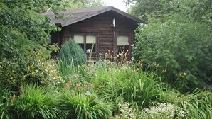 Una cabaña de madera rústica rodeada de exuberante vegetación y diversas plantas con flores.