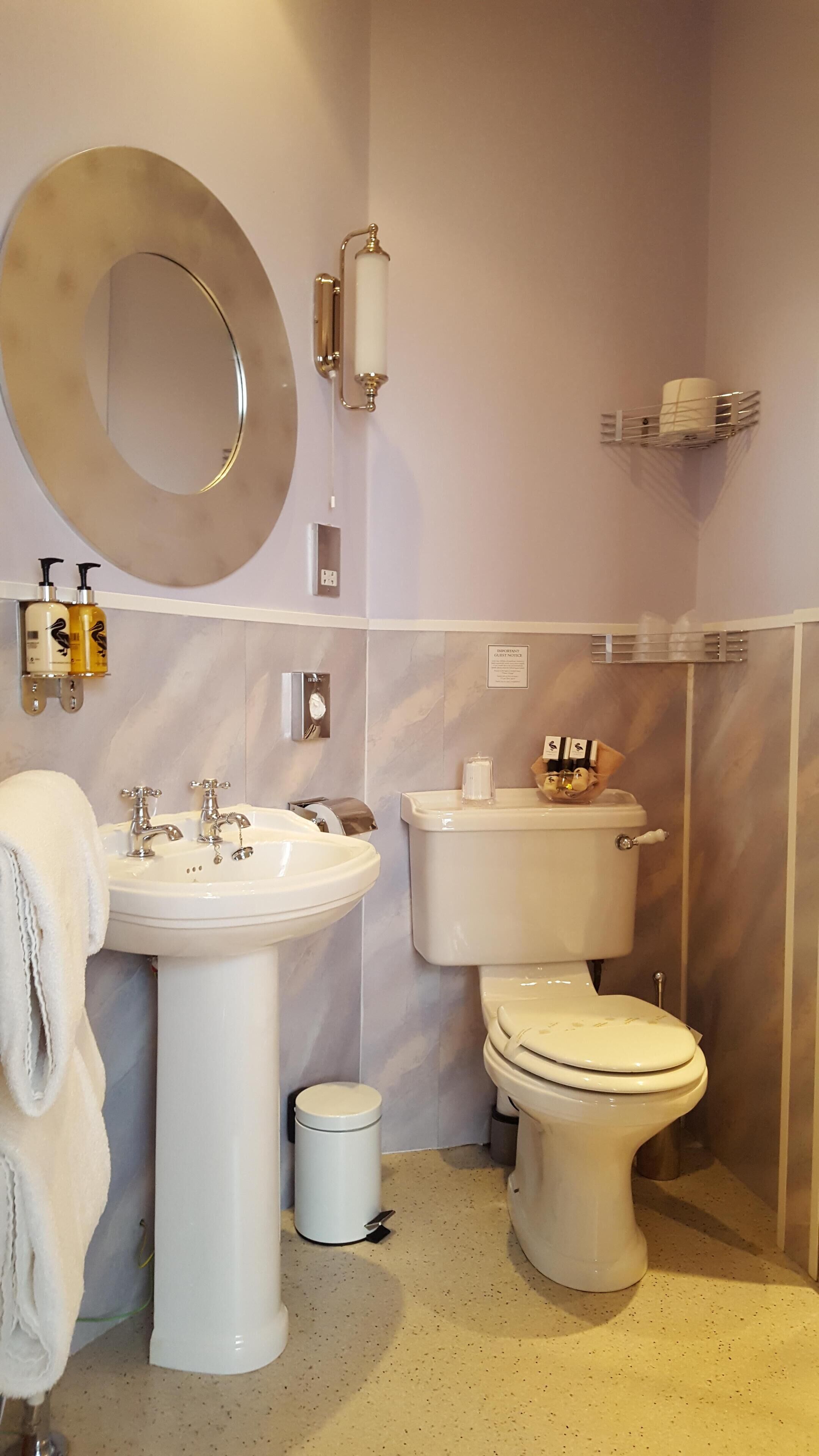 A bathroom with a sink, toilet, and bidet. There is a mirror, a towel, and toiletries on the wall.