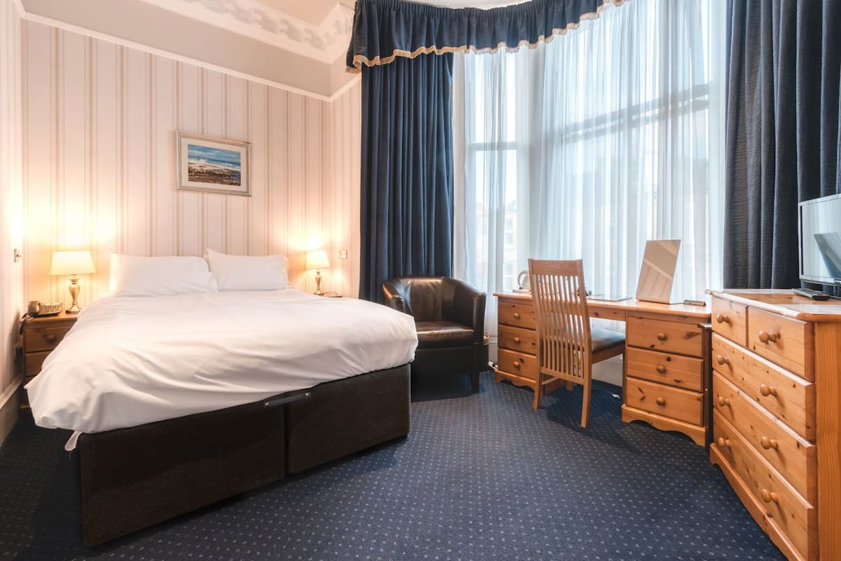 A hotel room with a bed, a desk, a chair, a dresser, and a television.