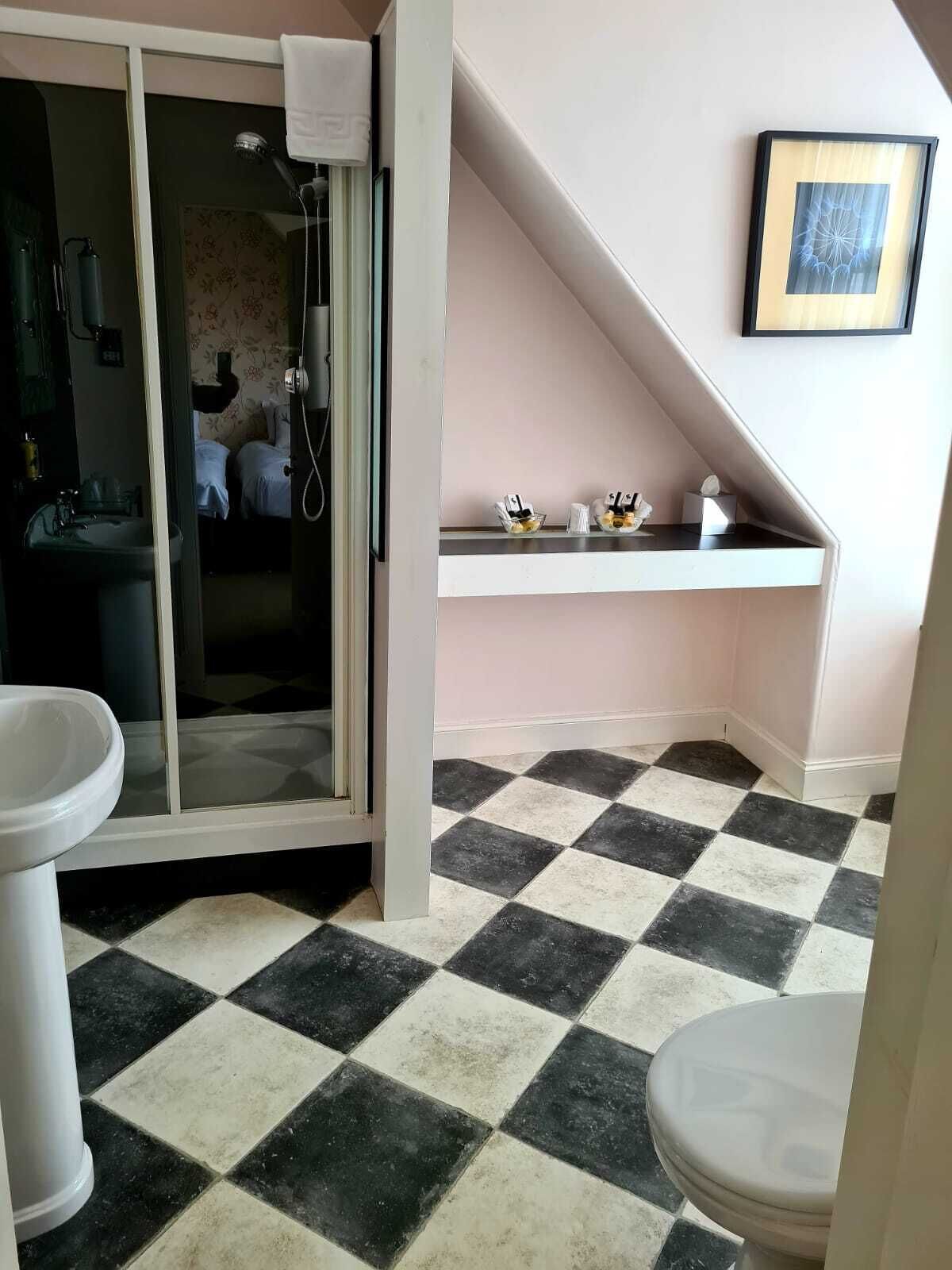 Et badeværelse med gulv i skakmønster, en bruser, en vask og et toilet.