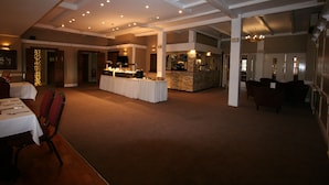 A spacious indoor area with a long table set for dining, a bar area with a stone counter, and a seating area with chairs. - Grange Moor Hotel (Maidstone)