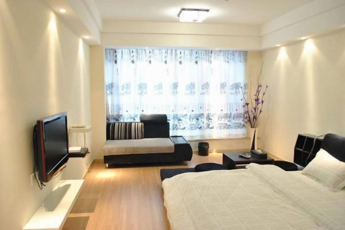 A modern bedroom with a bed, a sofa, a TV, and a window with curtains.