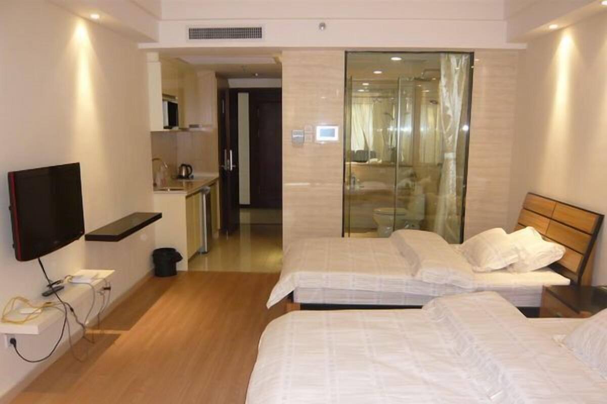 A hotel room with two beds, a TV, a small kitchenette, and a glass shower enclosure.