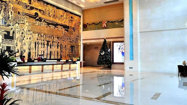 A spacious lobby with a large, ornate mural on the wall, a Christmas tree, and a reception desk. - Vili International Hotel (Guangzhou)
