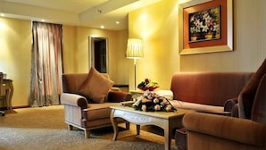 A hotel room with a sofa, armchair, and a coffee table with a floral arrangement. - Vili International Hotel (Guangzhou)