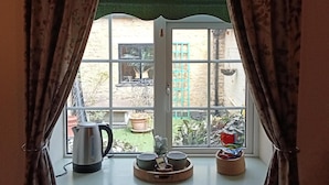 A window with curtains, a kettle, and a tray with bowls on a windowsill.