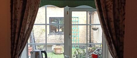 A window with curtains, a kettle, and a tray with bowls on a windowsill.