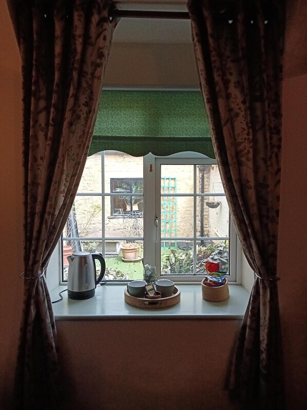 A window with curtains, a kettle, and a tray with bowls on a windowsill.