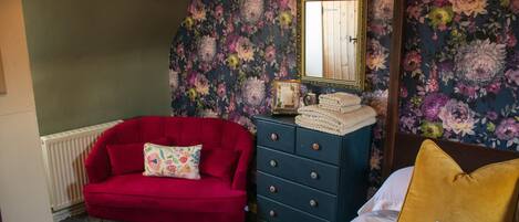 A bedroom with a red sofa, a dresser, a bed with a yellow pillow, and floral wallpaper.