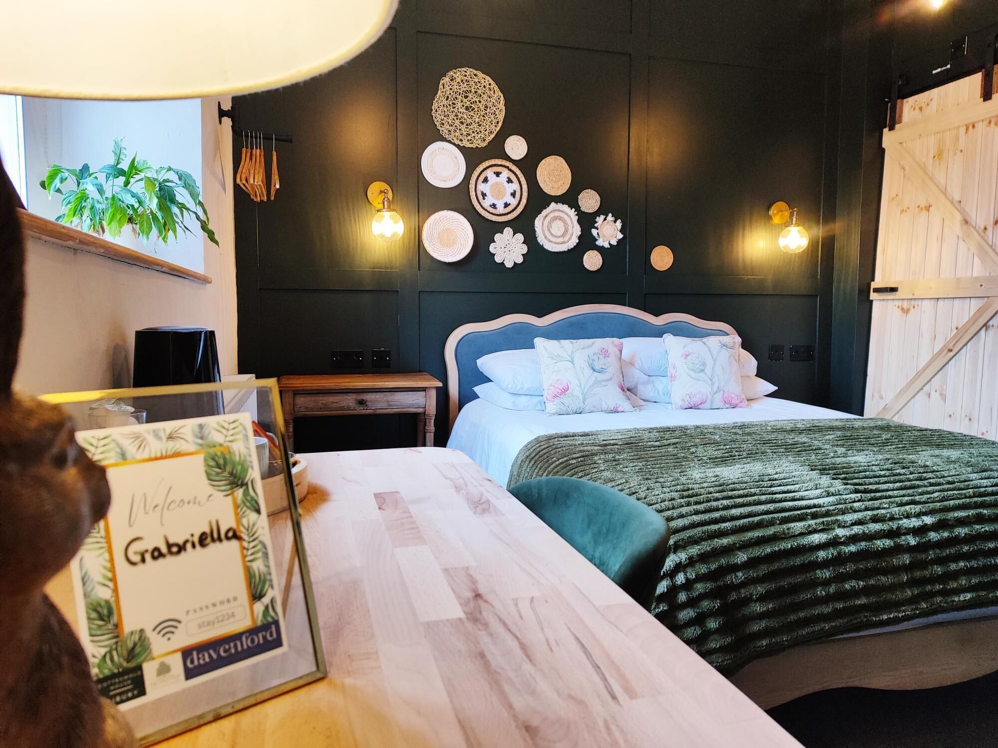 A bedroom with a bed, bedside tables, a wall-mounted lamp, and a framed welcome sign.