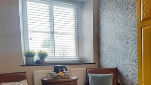 A room with two brown leather chairs, a small round table with a kettle and a plate, and a window with blinds.