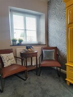 Una habitación con dos sillones de cuero marrón, una mesita redonda con una tetera y un plato, y una ventana con persianas.