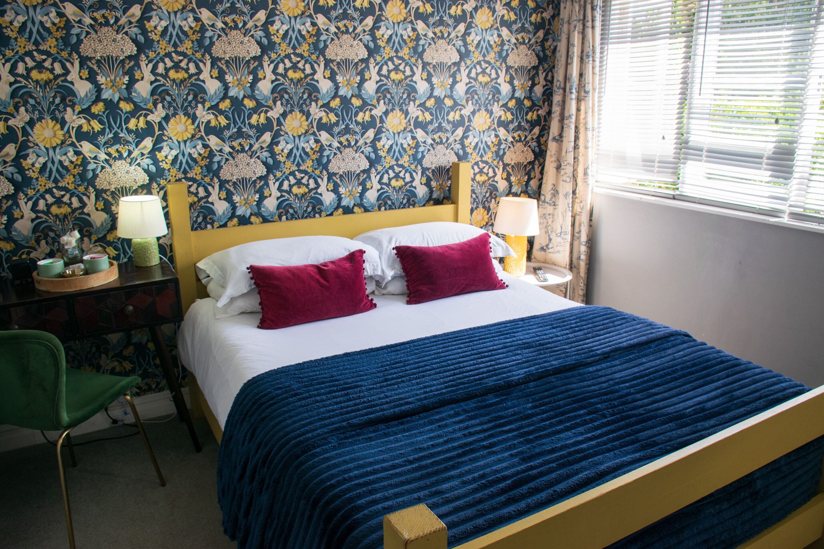 Ein Bett mit blauer Decke, zwei Kissen und einem floralen Wandmuster.