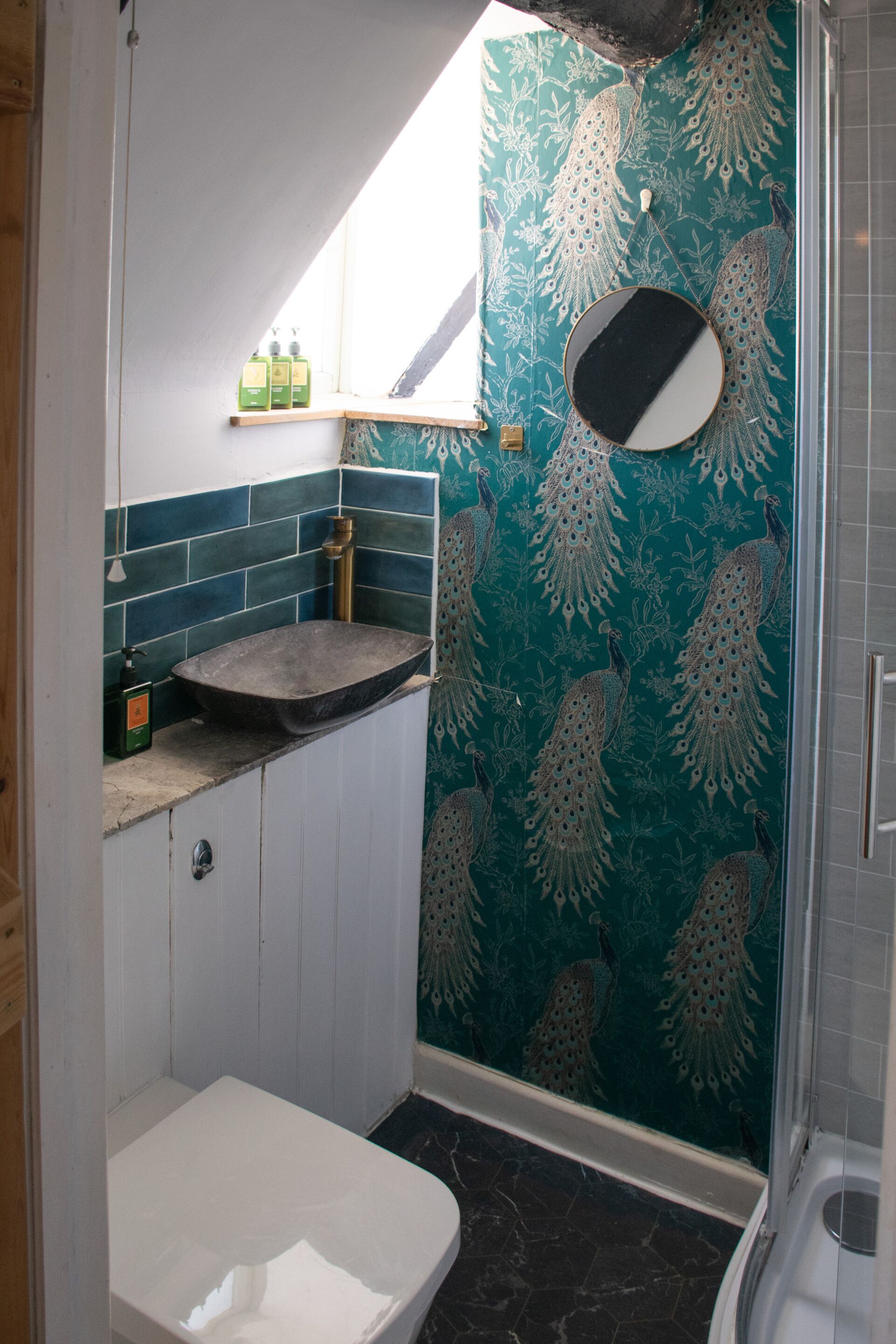 A bathroom with a peacock-themed wall, a sink with a marble countertop, and a shower area.