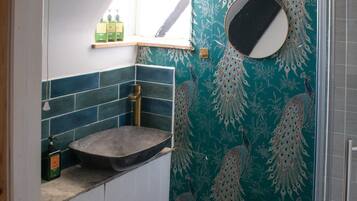 A bathroom with a peacock-themed wall, a sink with a marble countertop, and a shower area.