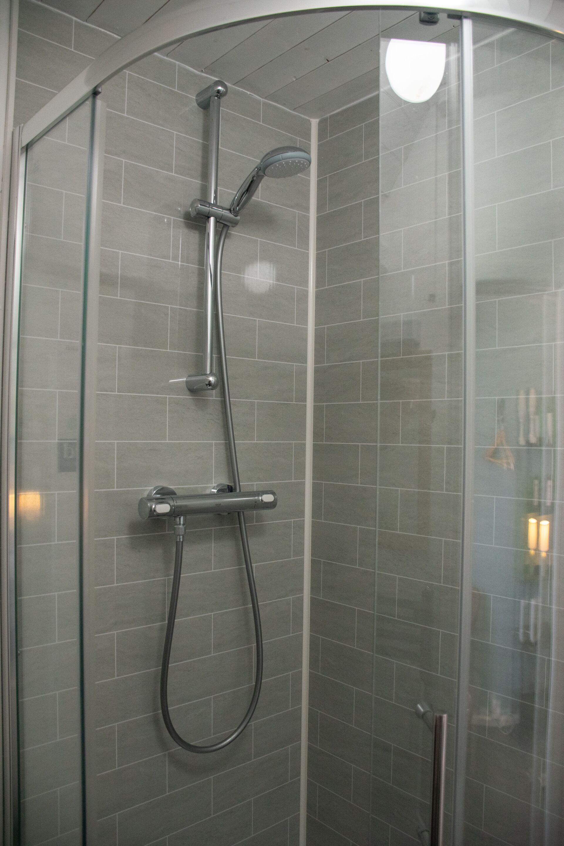 Une cabine de douche fermée par des parois en verre, équipée d’un pommeau de douche à main et d’un pommeau de douche fixe.