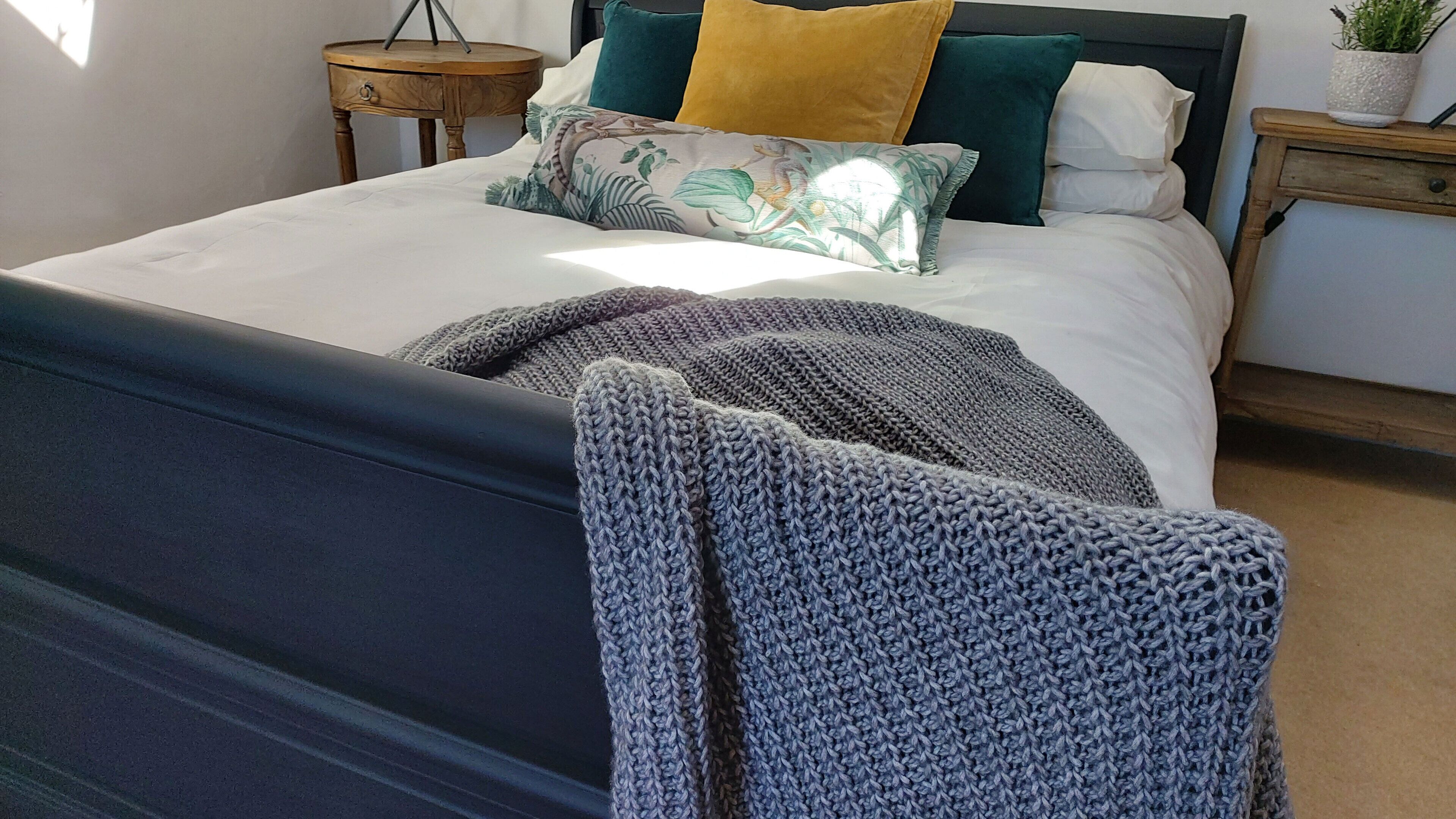 A neatly made bed with a dark headboard, multiple pillows, and a knitted blanket.