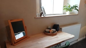 A wooden desk with a chalkboard, a coffee maker, and a small plant by a window.