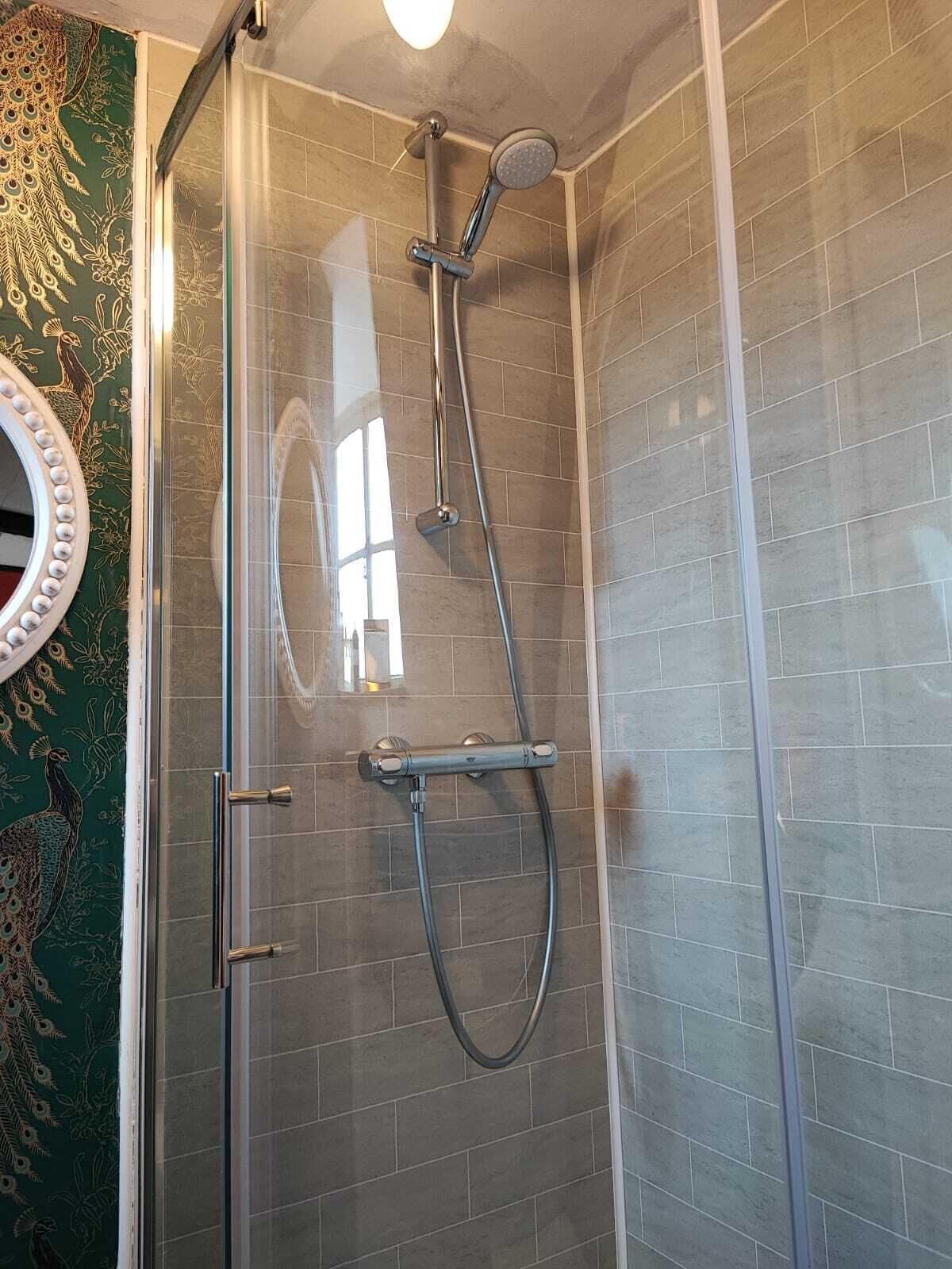 A shower with a glass door, a handheld showerhead, and a wall-mounted faucet.