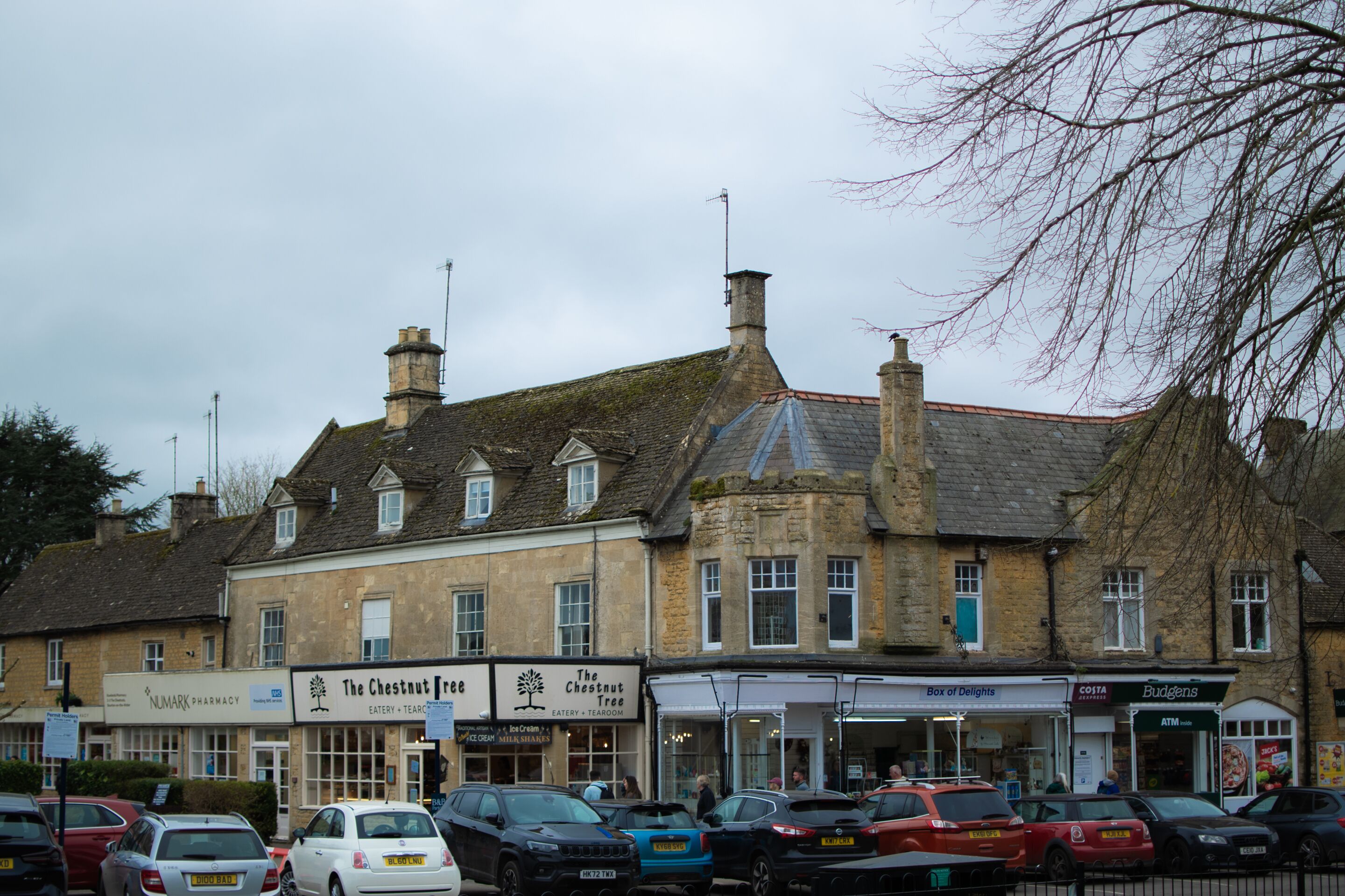A multi-story building with commercial establishments on the ground floor, including a pharmacy, a tearoom, and a cafe.