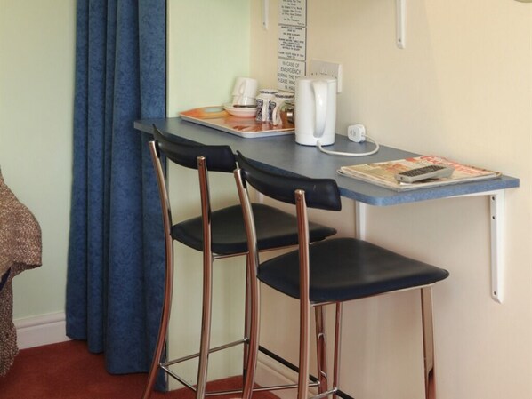 Una pequeña cocina americana con una mesa, dos taburetes altos, una cafetera, un hervidor y un microondas.