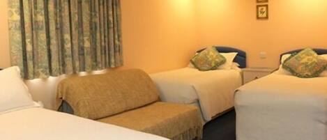 Habitación de hotel con dos camas individuales, un sofá y un ventanal grande con cortinas.