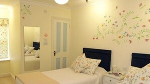 A bedroom with two beds, a nightstand, a mirror, and floral wall art. - Little Bullocks Farm (Bishop's Stortford)