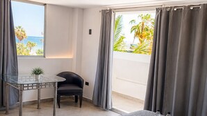 Ein Hotelzimmer mit Bett, Schreibtisch, Stuhl, einem Fenster mit Vorhängen und Blick auf Palmen.
