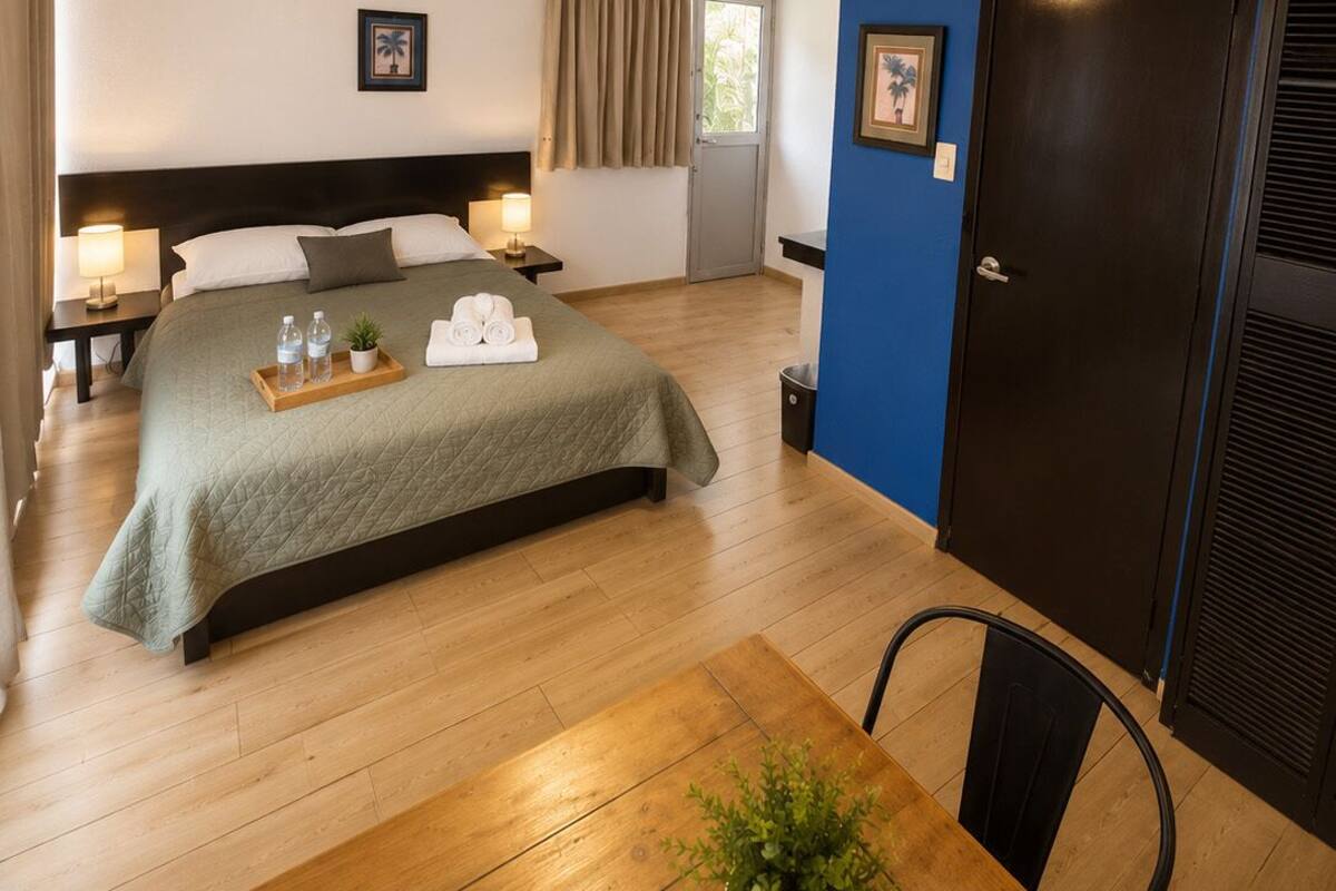 Habitación de hotel con cama, lámparas de noche, una mesa con planta y una puerta.