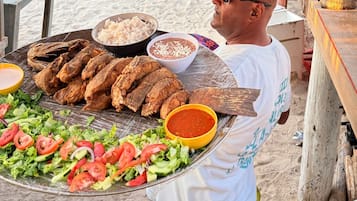 Una persona lleva una bandeja con pescado a la parrilla, arroz, ensalada y salsas.