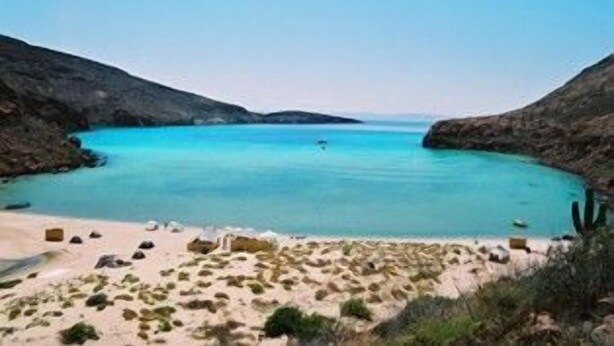 Eine Küstenlandschaft mit blauem Meer, Sandstrand und steilen Felsen.