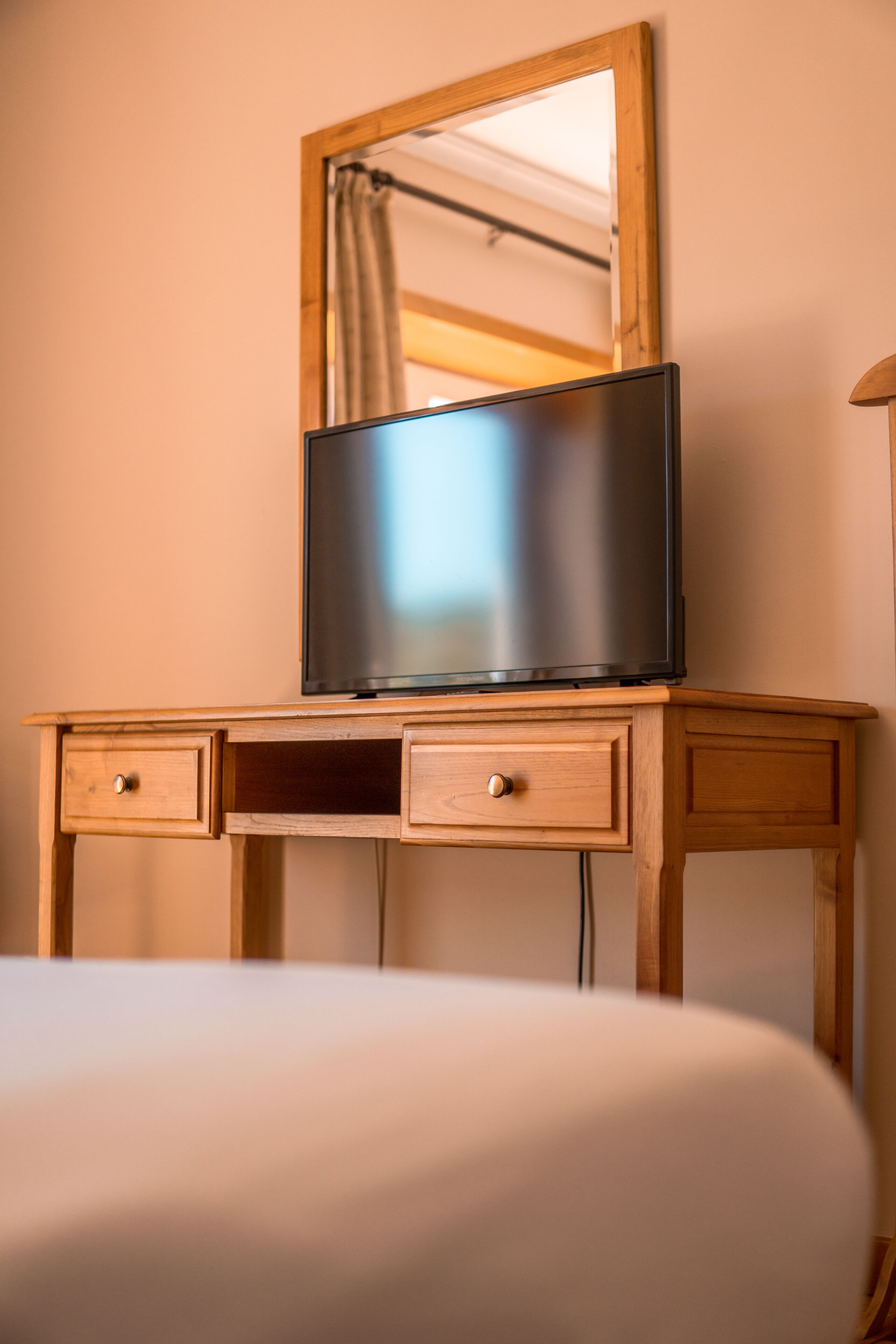 A wooden bedside table with a flat-screen TV and two drawers.