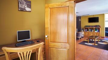 A room with a wooden desk, computer, and chair, a bookshelf, and a television on the wall.