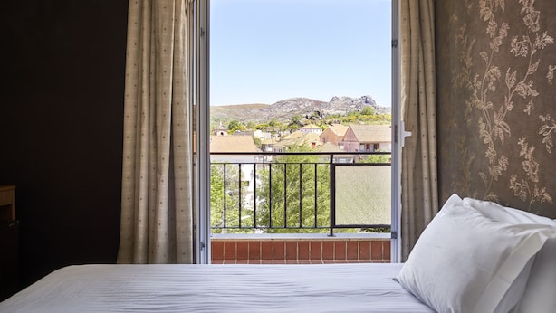 A bedroom with a bed, curtains, and a view of a mountainous landscape through a balcony.