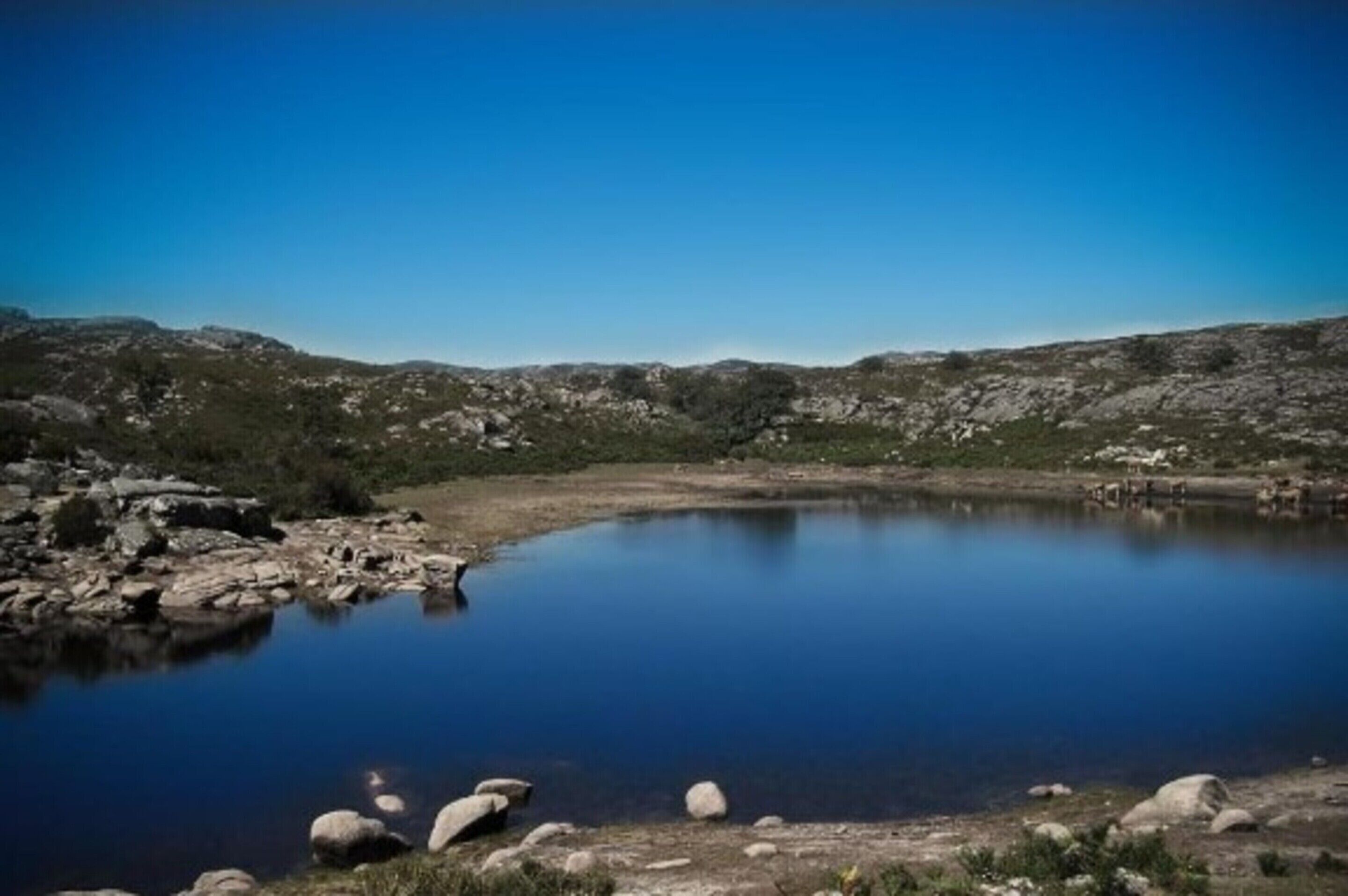 A natural landscape with a calm lake surrounded by rocky terrain and sparse vegetation.