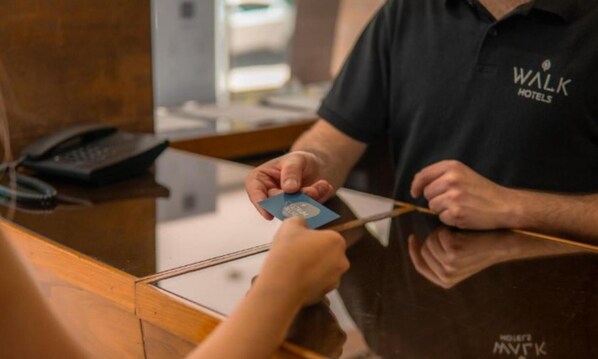 Una persona al taulell de recepció d'un hotel agafant una targeta, amb un telèfon i una bossa negra al mostrador.