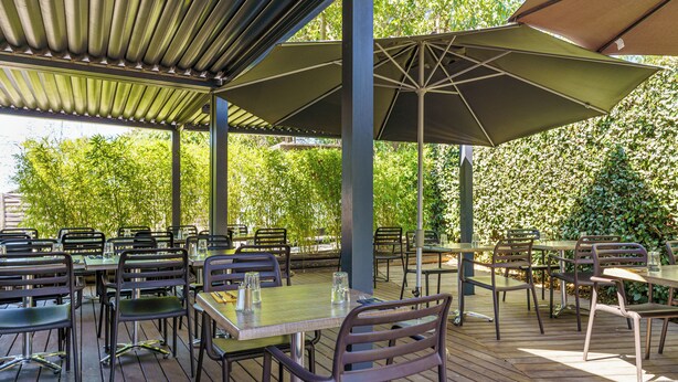 An outdoor patio with tables and chairs, covered by a roof and umbrellas. - Brit Hotel Confort Manosque Cadarache (Manosque)