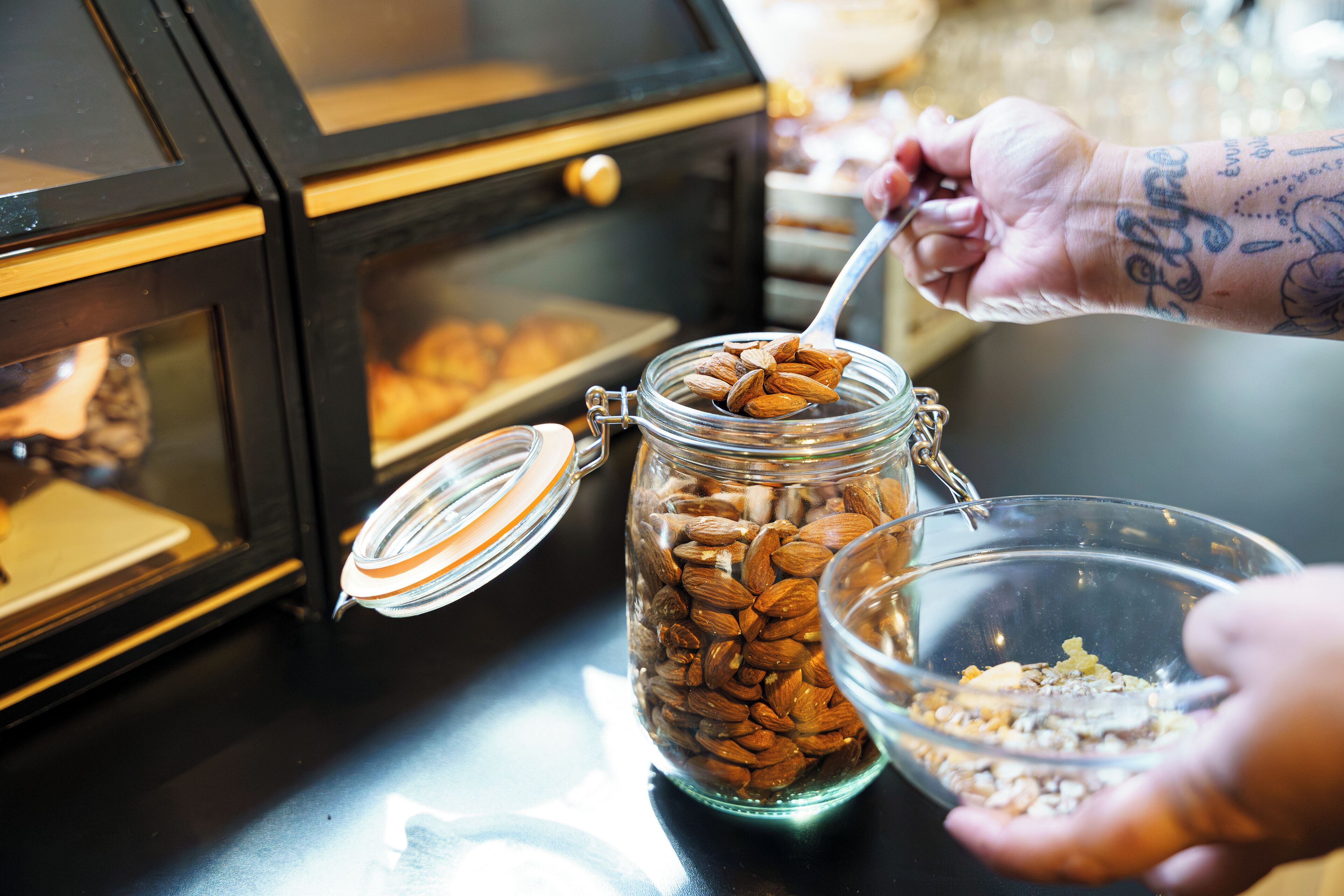 A person scooping almonds from a jar into a bowl.