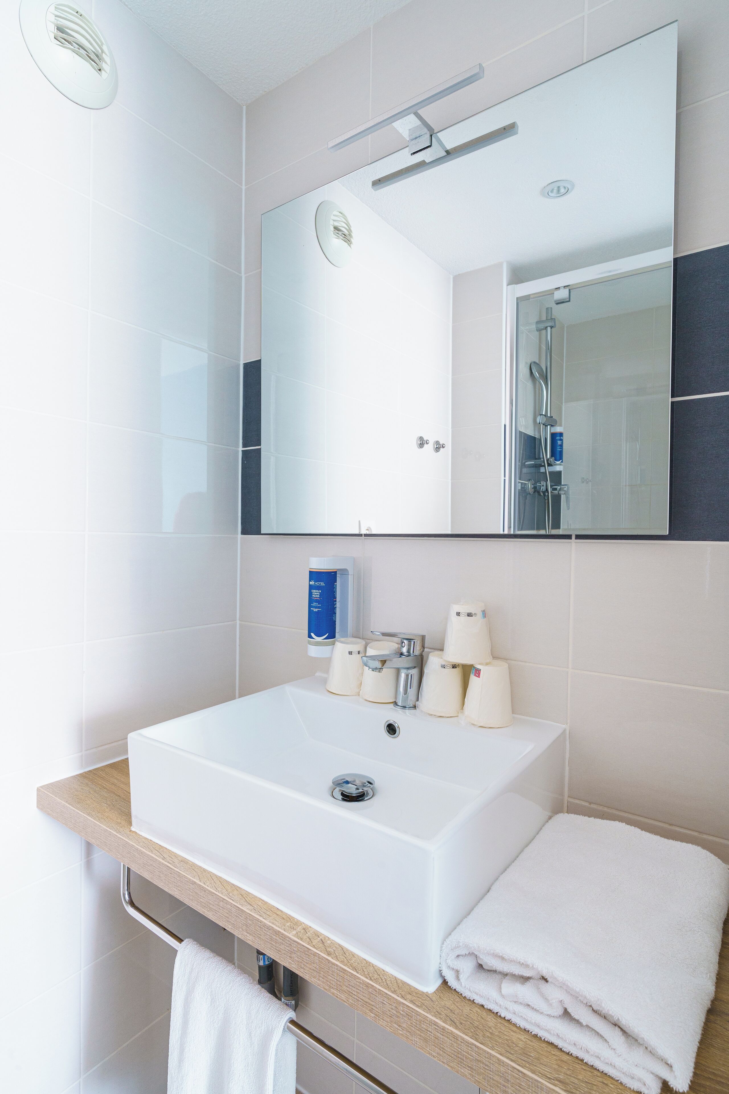 A modern bathroom with a large mirror, a white sink, and a towel on the counter.