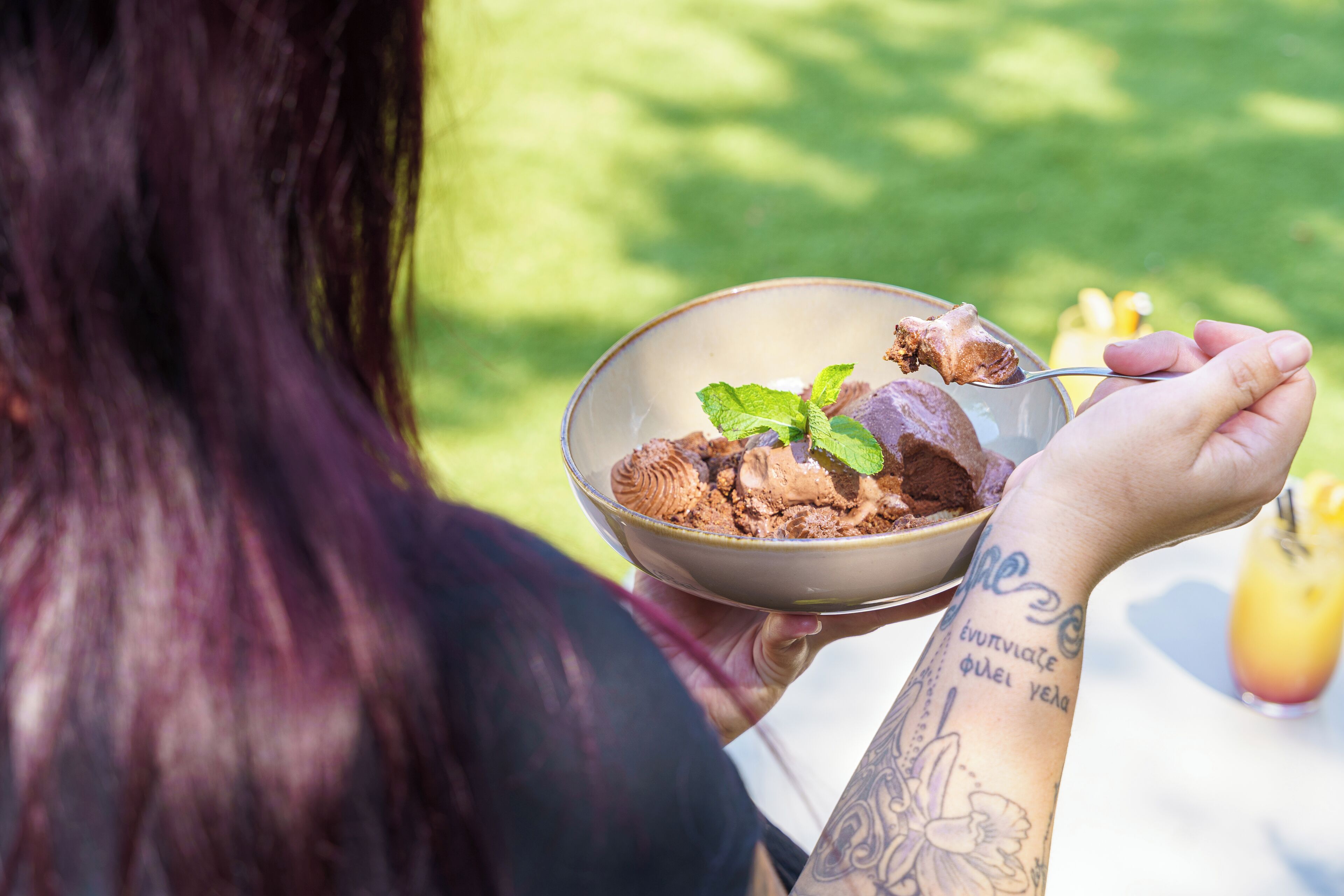 A person holding a bowl of ice cream with a mint leaf on top, outdoors.