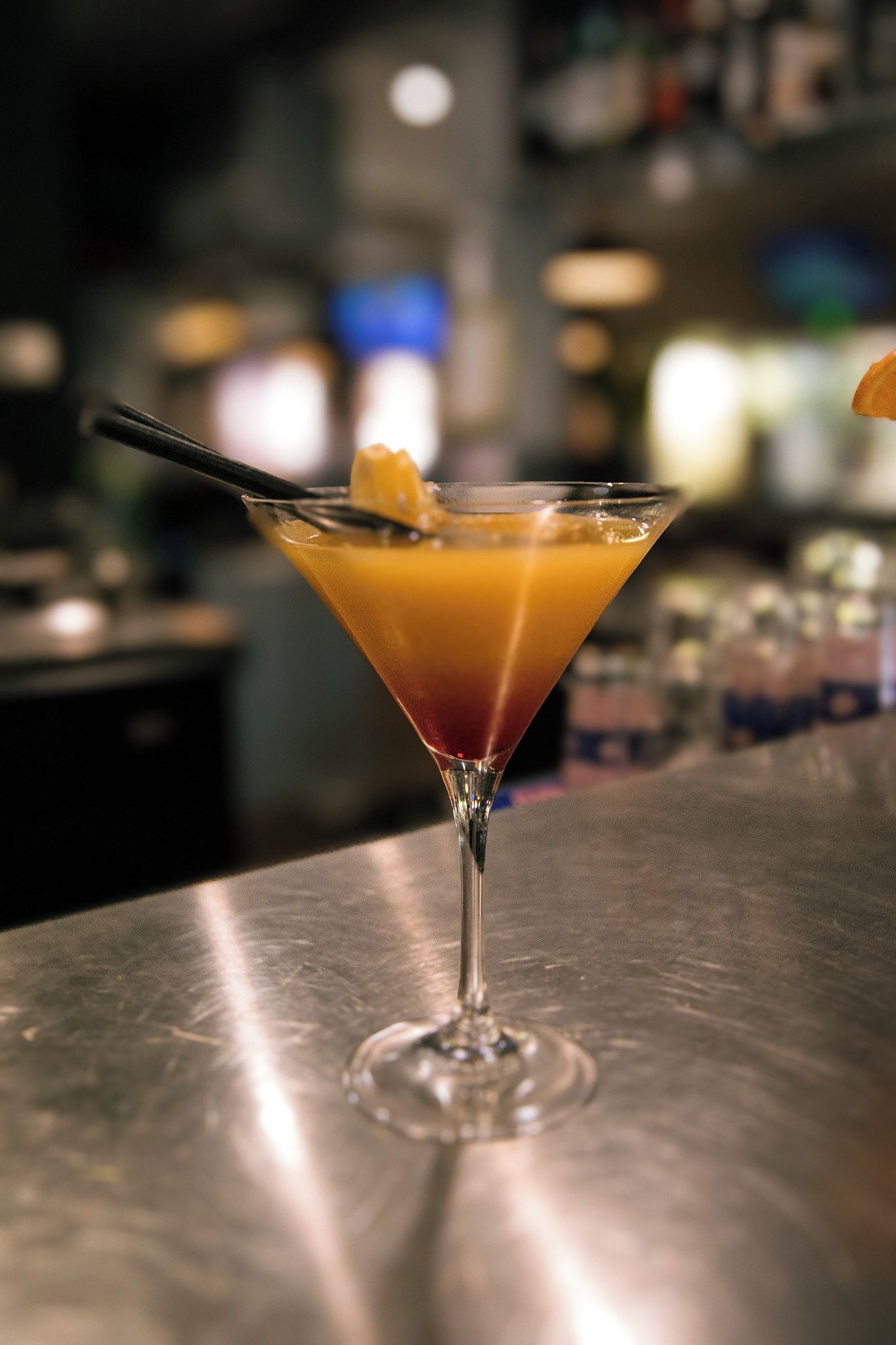 A martini glass with a layered drink on a bar counter.
