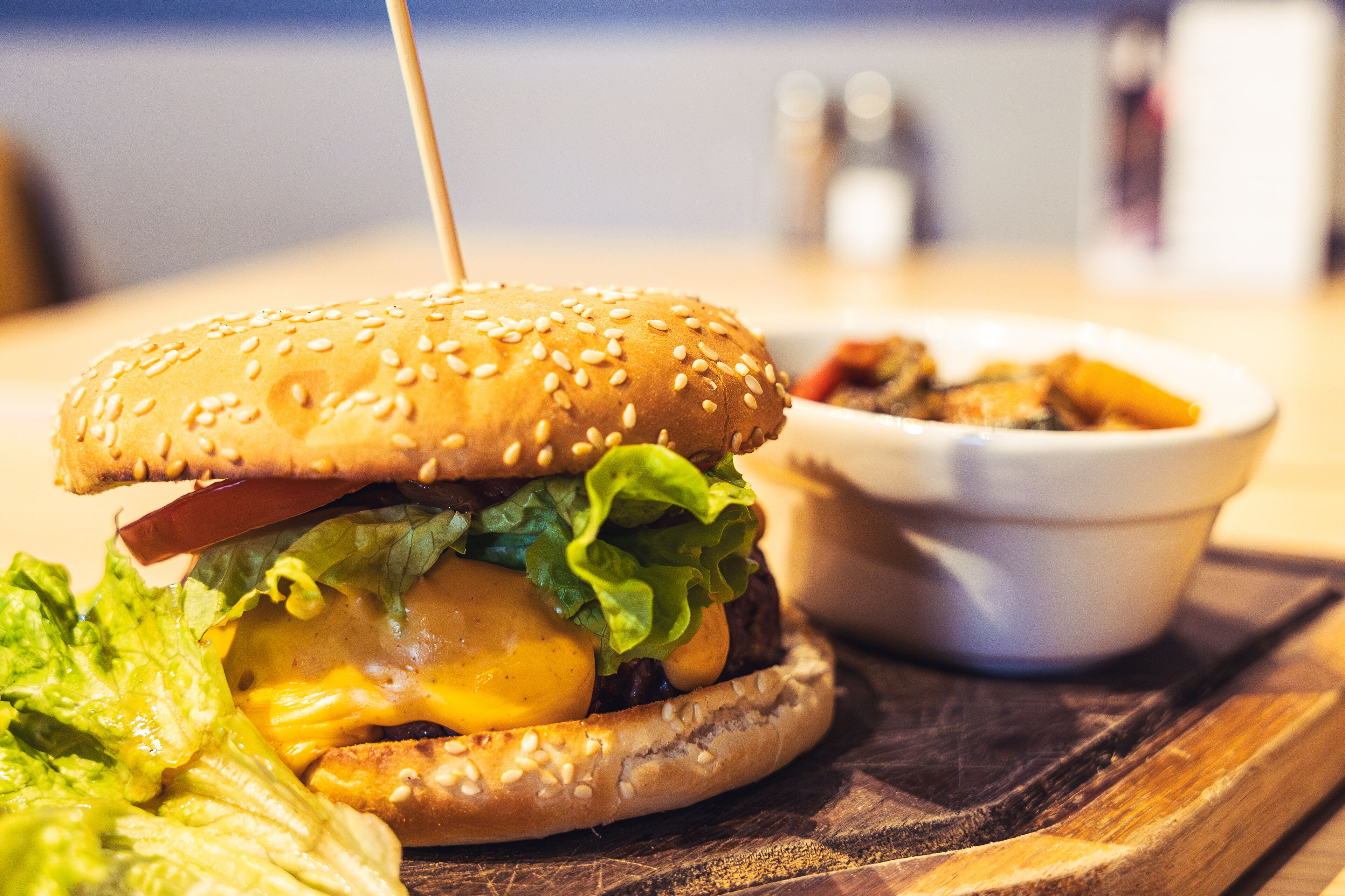 A burger with a sesame seed bun, lettuce, cheese, and a tomato, served with a side of fries and a small bowl of sauce.