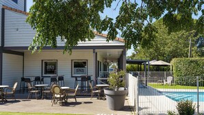 An outdoor seating area with tables and chairs, a pool, and a sign for 'SENZO Pizza - Grill'. - Brit Hotel Confort Manosque Cadarache (Manosque)