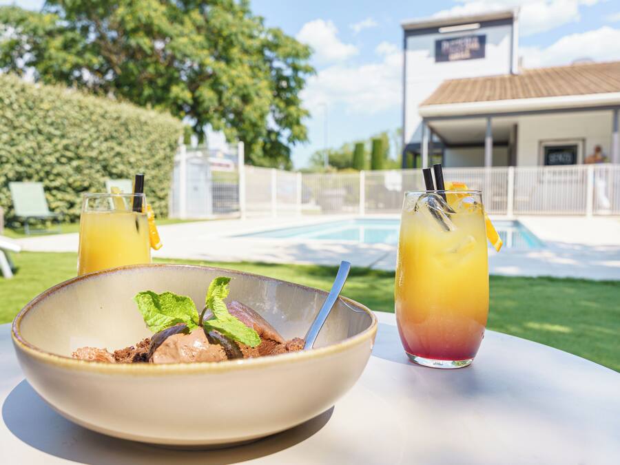 Una mesa de comedor con un tazón de postre y dos bebidas, una piscina y un edificio al fondo.