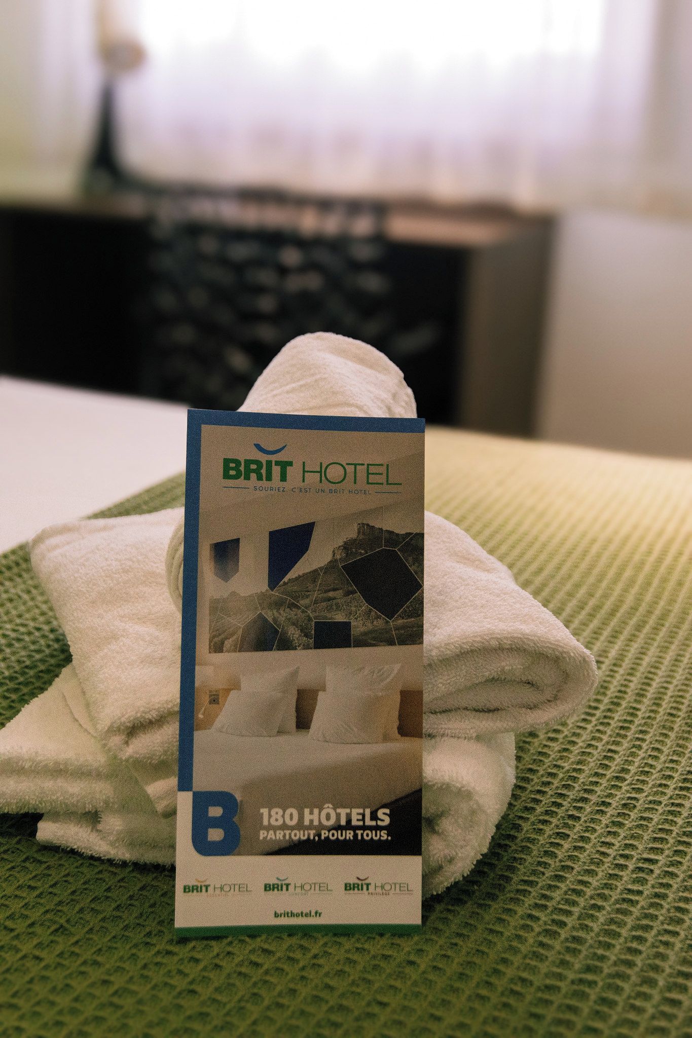 A rolled towel on a textured surface with a Brit Hotel brochure.