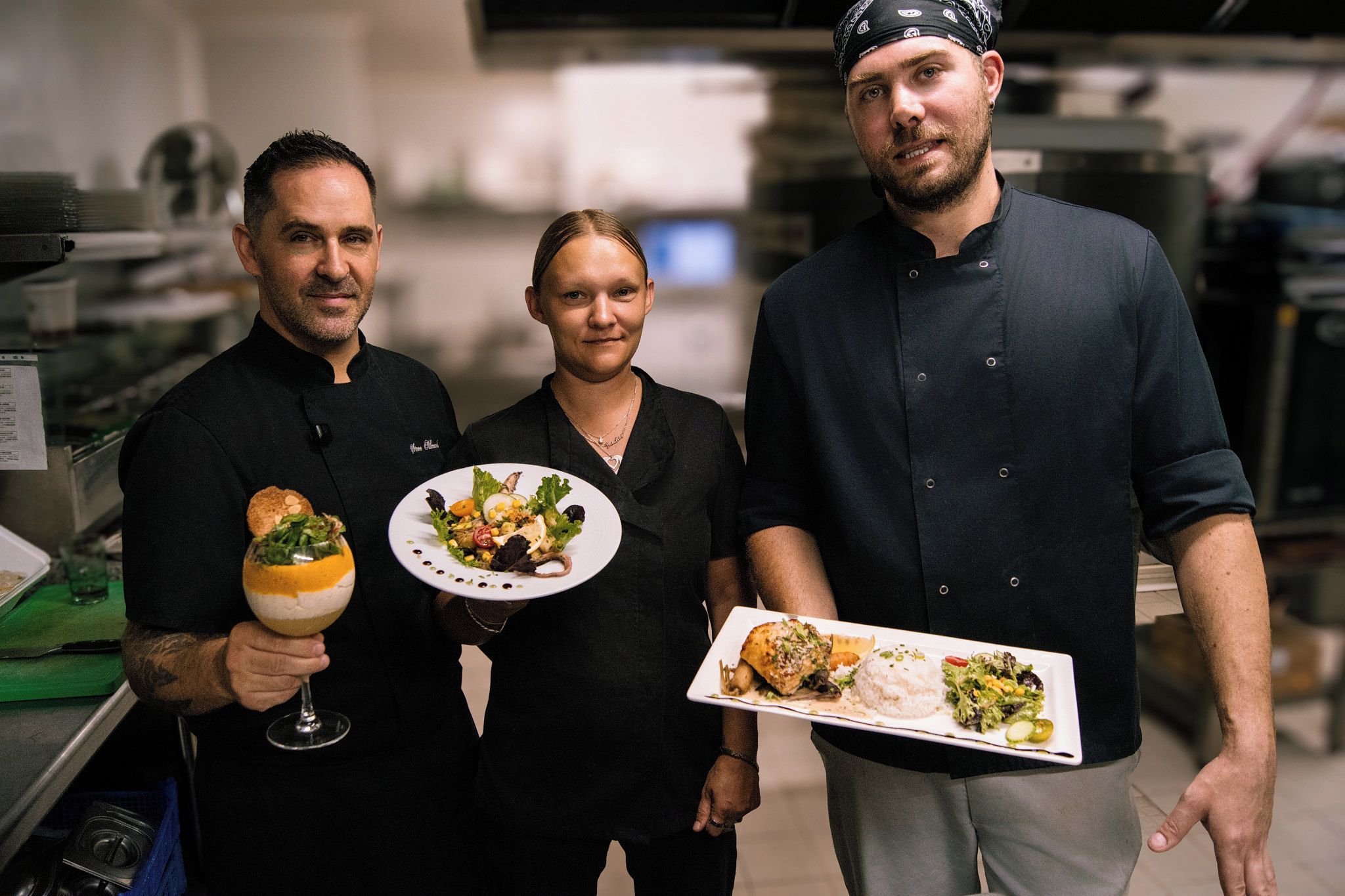 Trois personnes, chacune tenant une assiette de nourriture, dans une cuisine.